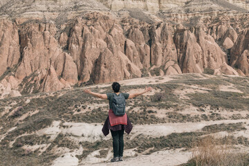 Woman with backpack opening her arms in front of a rocky mountain in Cappadocia, Turkey