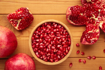 Open pomegranates, and pomegranate seeds in bowl on wooden background.