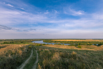Fototapeta premium A road winds through a grassy field with a river in the distance