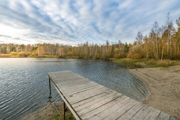 A wooden pier sits on the edge of a lake, with a cloudy sky overhead