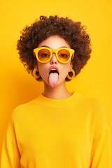 sassy young woman sticking out tongue wearing yellow glasses and sweater