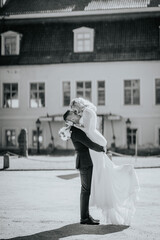 Black and white photo of groom lifting bride in an embrace, sharing a joyful kiss outside an...