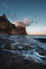 The rock rises above the blue sea at sunset or sunrise