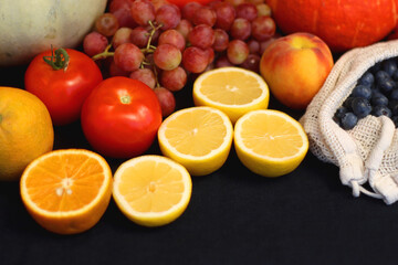 Round straw bag and various seasonal fruits and vegetables on dark background. Summer and fall produce. Selective focus.