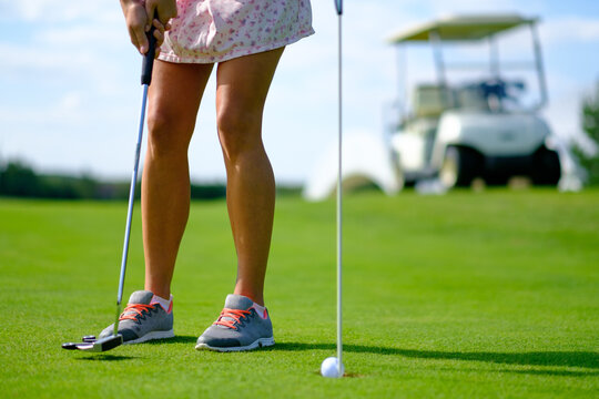 A woman prepares to putt on a sunny golf course while a golf cart waits nearby concept - Powered by Adobe
