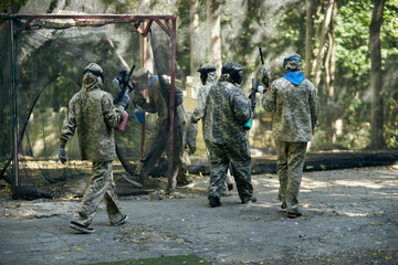 Paintball player in protective mask aims gun, takes cover under fire, paint splashes. Paintball player hide behind wooden barricade, shooting paintballs. Paintball players.