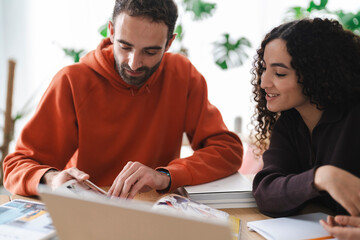 man wearing an orange hoodie is engaged in a conversation on his smartphone. He appears relaxed, standing in a well-lit room with greenery in the background, adding a cozy and modern feel to the image