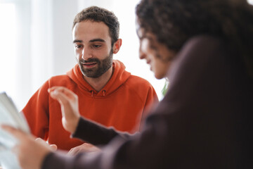 man and woman sit at a table with a laptop and books as they brainstorm ideas. They are having an in-depth conversation in a bright and modern space, symbolizing teamwork and creative collaboration.