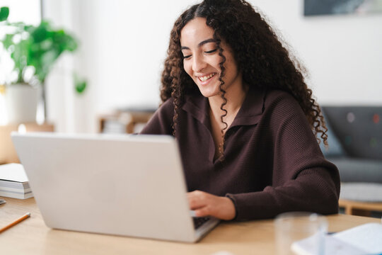 A young Arab woman with curly hair is deeply focused as she types on her laptop, creating a quiet and studious atmosphere at the table.
