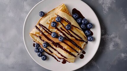 Crepes, thin pancakes with chocolate sauce and fresh blueberries. Grey background.