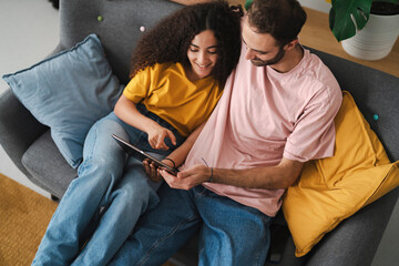 A relaxed couple sitting closely on a couch, engaged with a tablet, in a cozy living room adorned with indoor plants, creating a warm and welcoming atmosphere in a shared moment.
