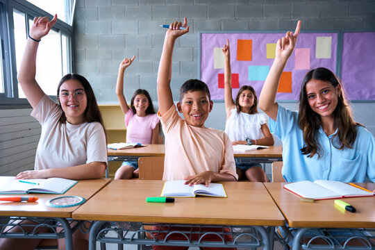 Portrait of happy group diverse elementary school students sitting in classroom with hands raised. Smiling Hispanic pre-teens children answering teacher question in class. Primary school concept