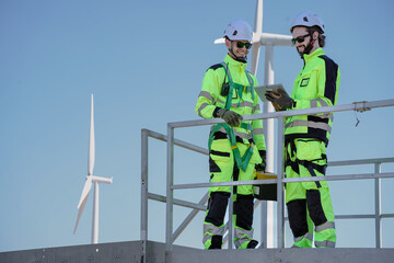 Maintenance engineer team standing at windmills at wind turbine farm. Skill people working outdoors at alternative renewable energy wind power station. Sustainable clean energy technology. Ecology