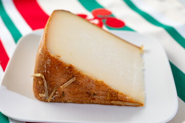 Piece of tasty Basque Brebis Fume smoked sheep cheese produced in south-western France, Northern Basque Country and towel with Basque symbol and colours