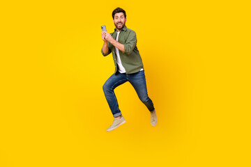 Fototapeta na wymiar Full length portrait of nice young man jump run smart phone wear shirt isolated on yellow color background