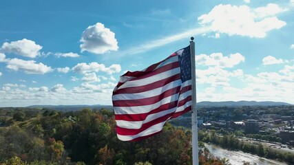 Patriotic American flag on flagpole moving over town.Sunny day in American city in fall season. Aerial close up orbit.Downtown with office buildings in background. Colored landscape of Connecticut. - Powered by Adobe