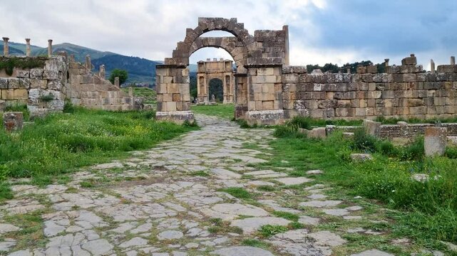 Revealing shot of arch gates and stone walls in the Roman ruins of Djemila in Algeria on a a cloudy day