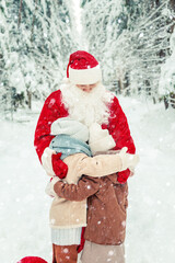 Joyful children hug Santa Claus in a snowy forest.