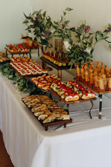 A wide selection of sandwiches and other snacks on the table. Table coasters with snacks decorated with fresh flowers.