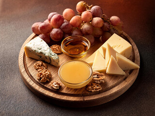 Una tabla de quesos, nueces y uvas, sobre una mesa de madera frente a una ventana luminosa con vistas al paisaje de oto&ntilde;o