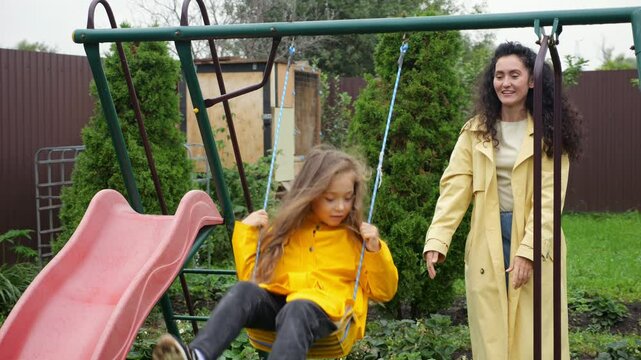 Mother joyfully pushing her daughter on a swing in the backyard playground