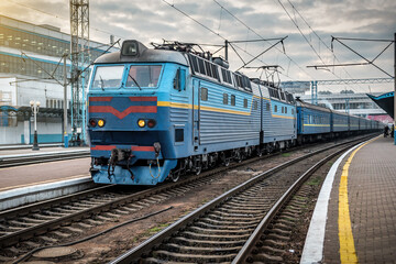 Electric locomotive with a passenger train on the station at sunset