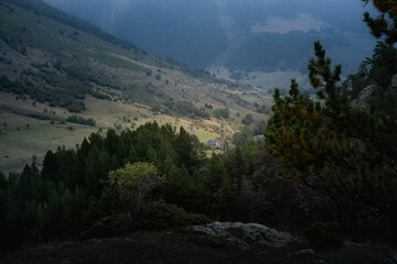 Panoramic view of the Aran Valley in the Spanish province of Catalonia. The day is dark and cloudy and at the bottom of the valley you can see the small Sanctuary of Montgarri with its tower