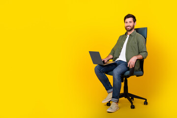 Full size photo of nice young man sit chair use netbook wear shirt isolated on yellow color...
