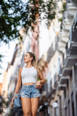 Young woman is walking down a city street during the day, holding a purse and smiling