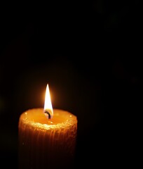 One lit candle burns brightly on a black background
