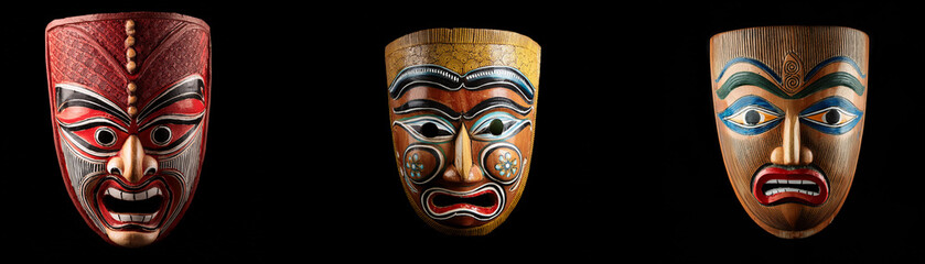 Three carved wooden masks are isolated against a black background.