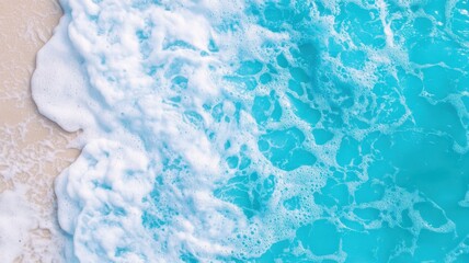 Obraz premium Aerial view of clear turquoise ocean waves gently lapping at a sandy beach, showcasing the vibrant colors of the water in a peaceful coastal setting.