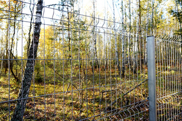 Obraz premium Fence for animal protection. Border as metal fence in forest. Fence with metal mesh in wildlife with trees. Protected area, restricted area, private property. Protect and ensure the safety of animals.
