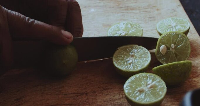 Beautiful close-up shot of an older latin woman cutting green lemons with pepa in half to prepare a sauce with onions in a stone kitchen inside a humble house in the highlands of Peru.