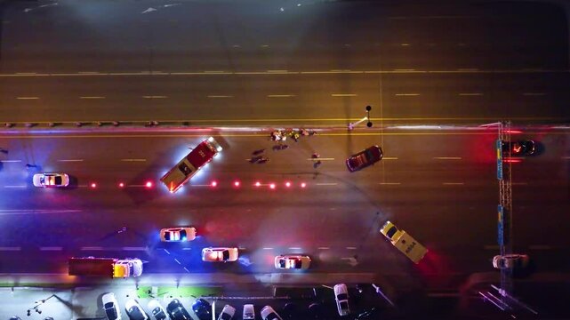 Pedestrian accident blocking lanes at night with emergency vehicles flashing lights and shutting down scene, drone top down