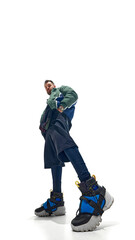 Low-angle shot of young man in layered outfit, with colorful sneakers and green bomber jacket against white studio background. Concept of fashion and style, beauty, trendy, freedom.