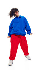 Low angle photo of carefree young woman in blue hoodie and red pants, smiling and shaking her hair against white studio background. Concept of fashion and style, beauty, trendy, glamour and emotions.