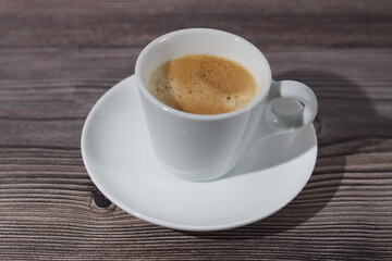 A white cup of espresso with its saucer on a wooden pattern.