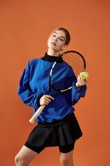 A passionate athlete poses with a tennis racquet and ball against a bright orange background.