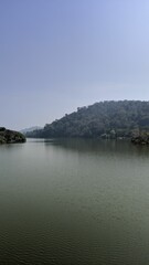 Serene lake surrounded by green hills under a clear sky.