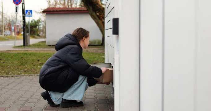 Brunette woman places parcel into matching locker finalizing shipping process. Lady deposits package into locker arranging return of online purchase