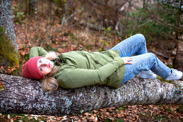 middle-aged caucasian man in hat and jacket is lying on the log in the autumn forest