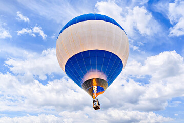 Colorful hot air balloon flying over blue sky with white clouds
