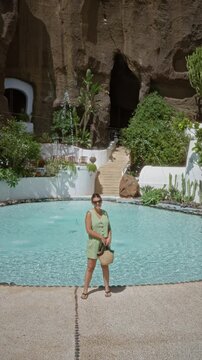 Woman standing in front of pool at lagomar lanzarote canary islands wearing green outfit holding bag with sunglasses enjoying sunny day near rock walls and tropical plants