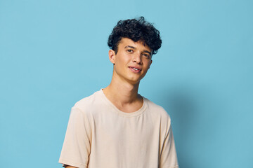 Portrait of a young man with curly hair, smiling against a pastel blue background, casual outfit conveying a relaxed and friendly vibe, ideal for lifestyle or personal branding concepts