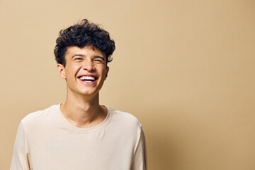 Young man smiling with curly hair, light shirt, cheerful expression against a warm beige...