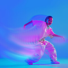 Creative design. Dynamic image of young woman in white clothes dancing hip hop with passion on blue...
