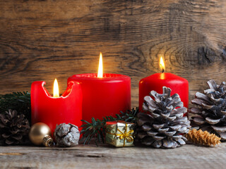 Red Advent candles on a rustic wooden background, third candle is burning
