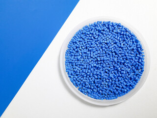 Blue masterbatch granules in a cup on a blue and white background, a color pigment carrier polymer...