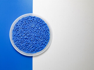 Blue masterbatch granules in a cup on a blue and white background, a color pigment carrier polymer in the plastics industry